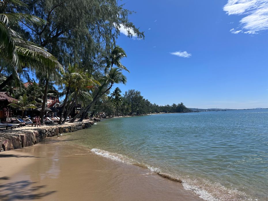 Palm-fringed beach with clear blue water in Phu Quoc, Vietnam, on a sunny day. Lounge chairs line the shore, capturing the relaxed vibe of solo travel in Phu Quoc.